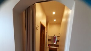 Un pasillo estrecho con una puerta al final, que da a un baño con un espejo y un lavamanos.
