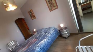 A bedroom with a bed, bedside tables, a chair, a hanging light fixture, and a door.