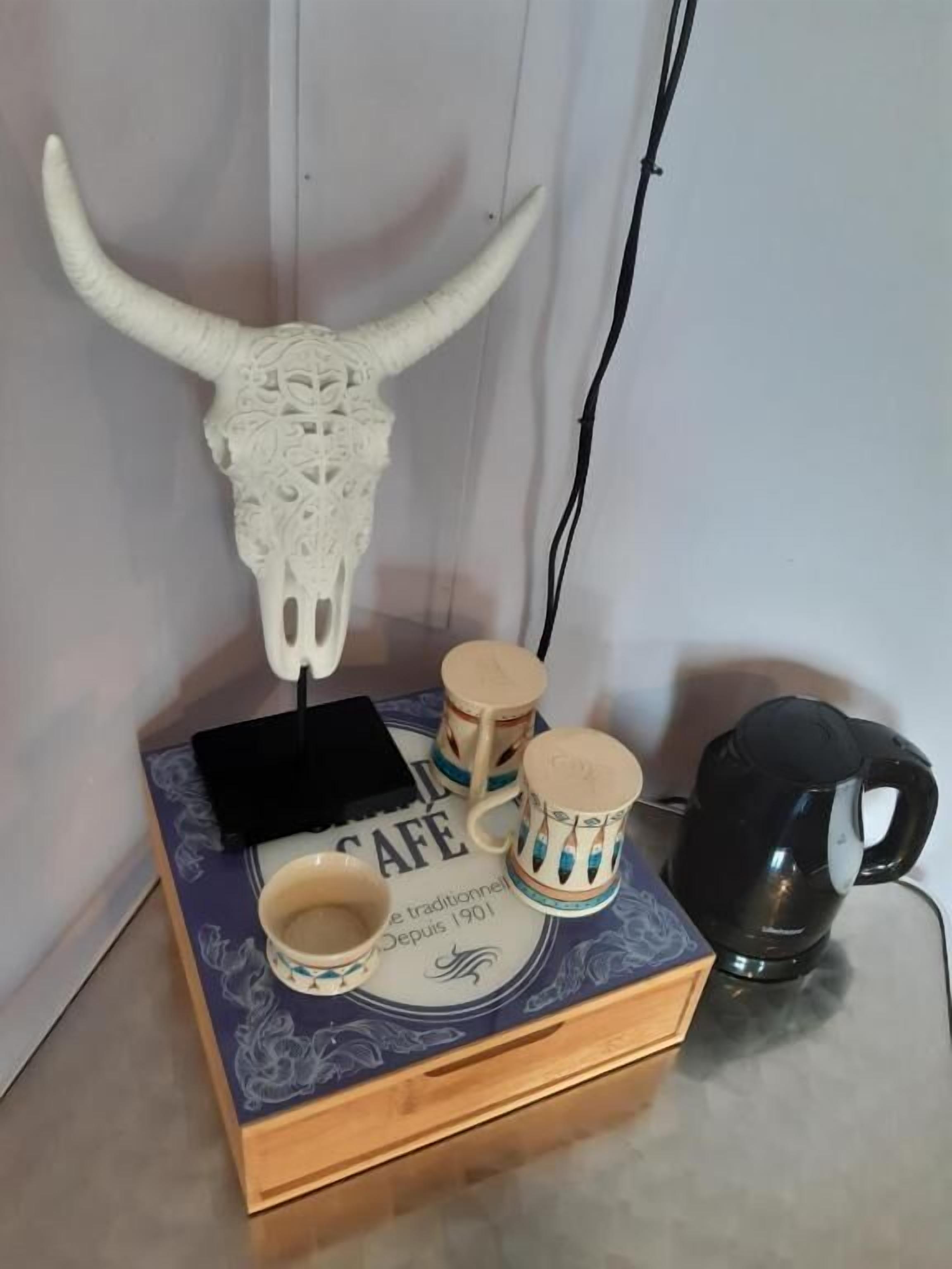 Un elemento decorativo a parete con un teschio di mucca e corna, un oggetto nero e due tazze di ceramica su una scatola con il cartello 'CAFE'.