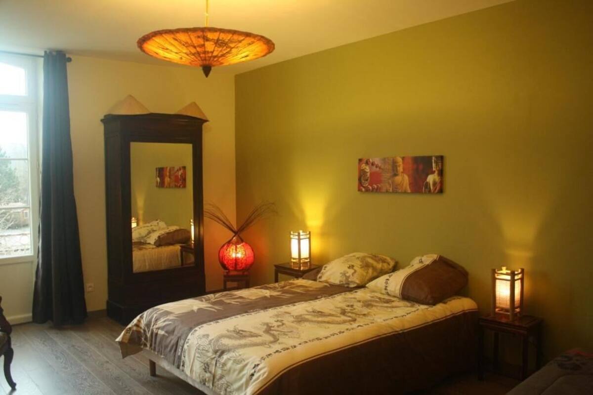 Une chambre à coucher avec un lit, un miroir, une lampe et des œuvres d’art accrochées au mur.