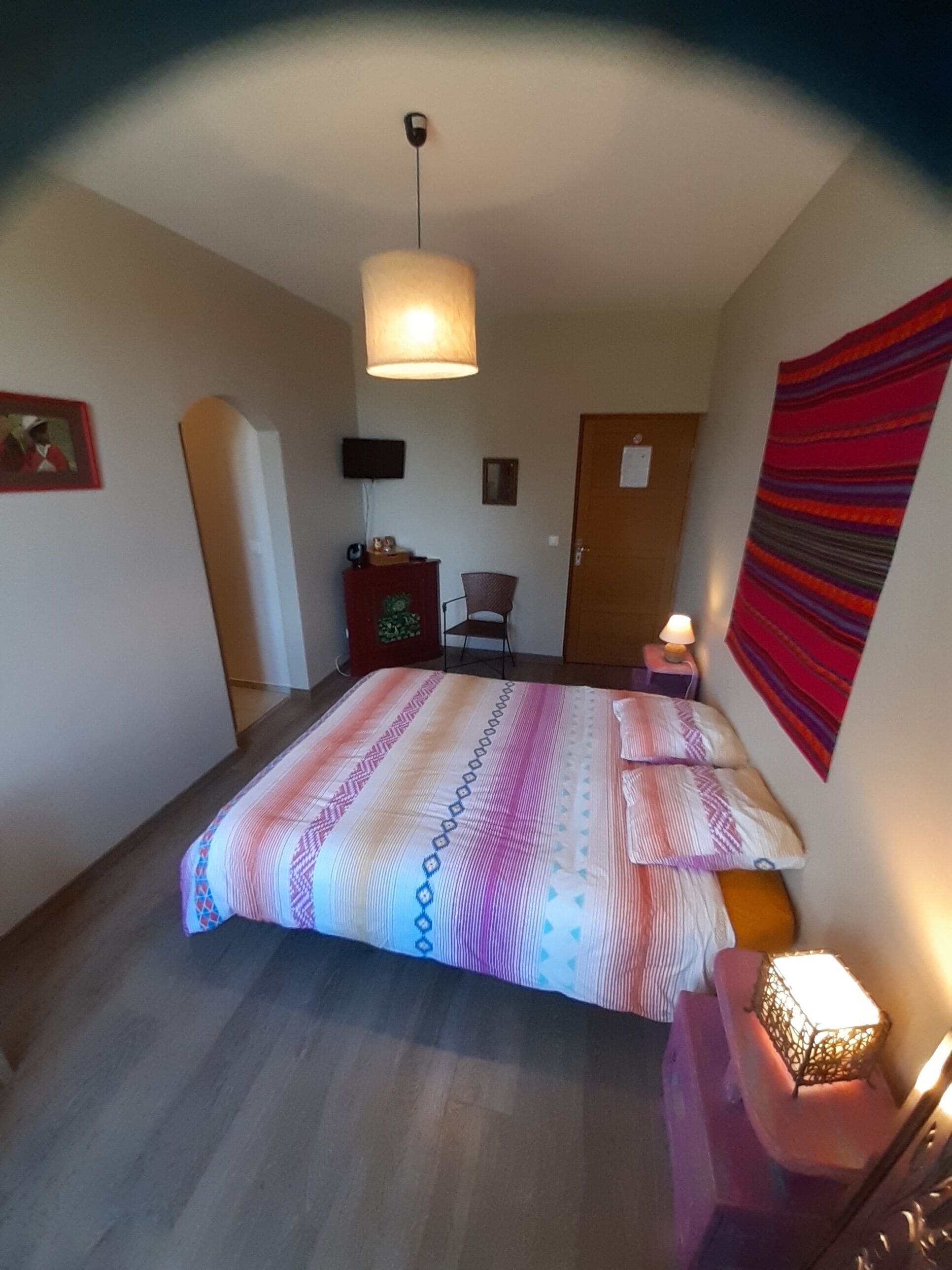 A bedroom with a bed, a desk, a chair, a lamp, and a door.