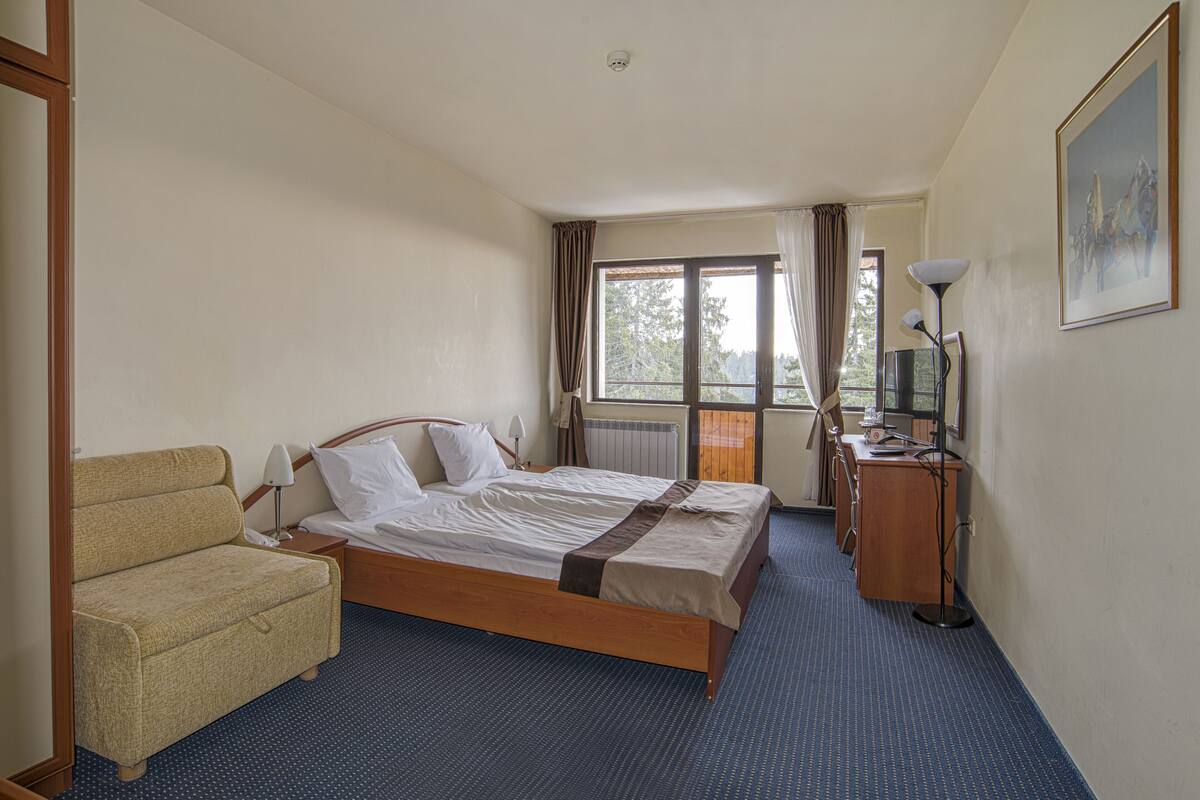 Ett hotellrum med en säng, en soffa, ett skrivbord, en lampa och en tavla på väggen.