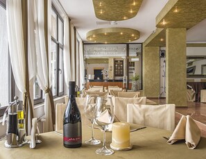 A restaurant interior with tables set for dining, a wine bottle, and glasses on the table. - Hotel Kamena Pamporovo (Chepelare)