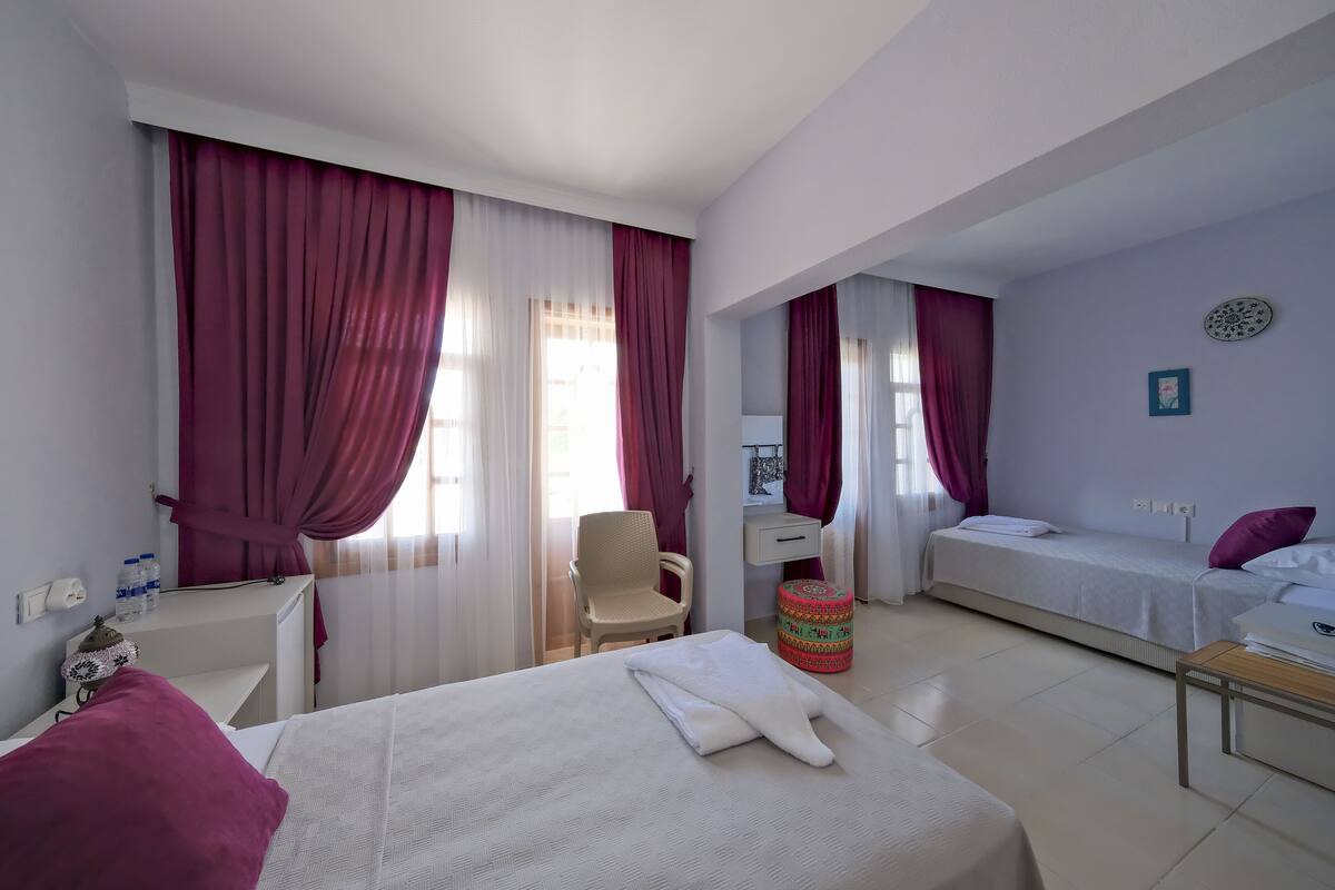 Une chambre d’hôtel avec un lit, un bureau, une chaise, une petite table et une fenêtre avec des rideaux.