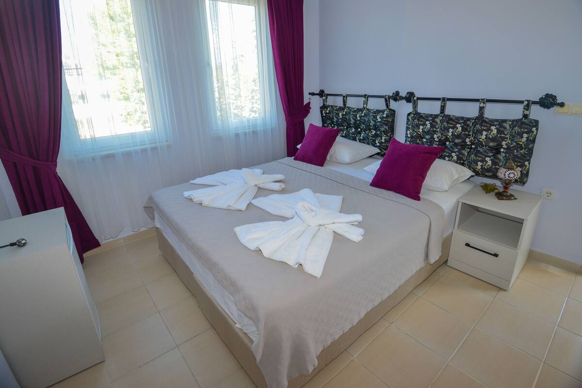 Une chambre d’hôtel avec un lit, une table de chevet, une commode et une fenêtre avec des rideaux.