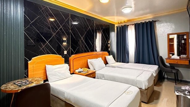 A hotel room with two beds, a desk, a chair, and a mirror. - Maaeen Hotel (Dubai)