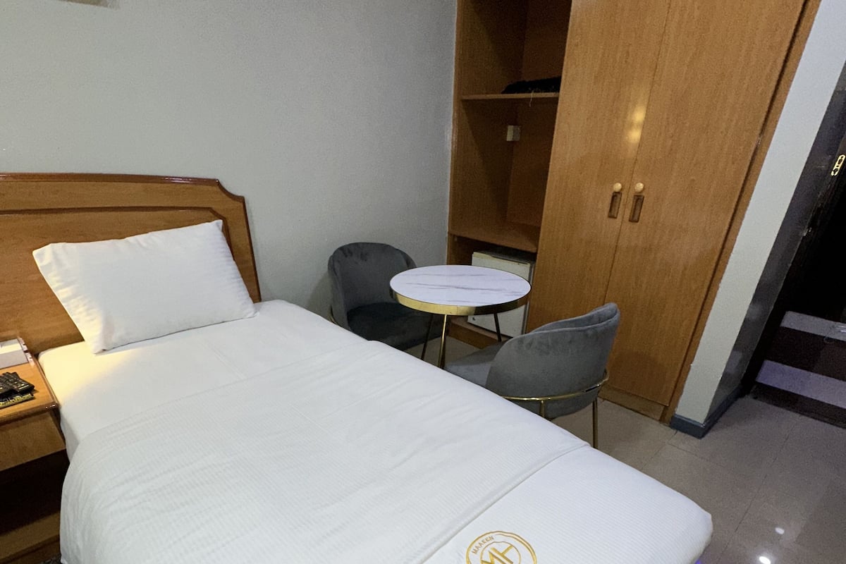 A hotel room with a bed, a small round table, a chair, and a wardrobe.