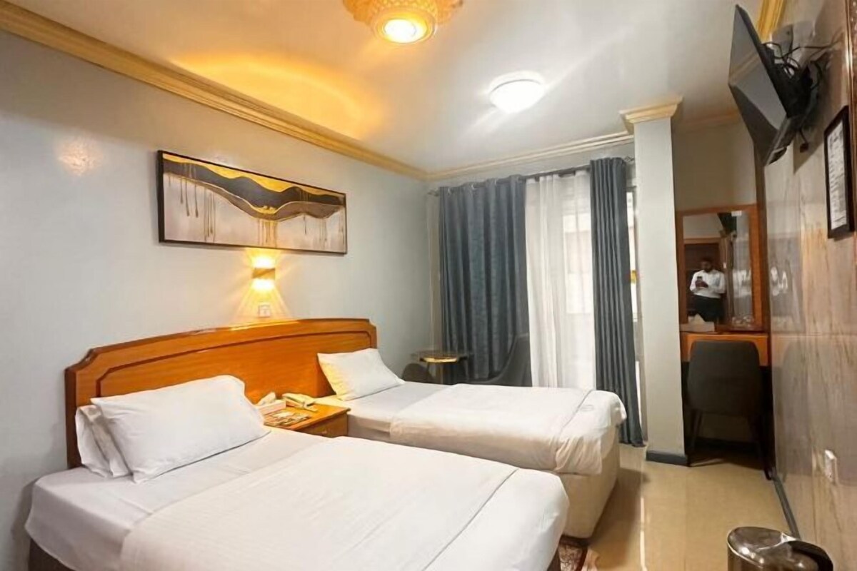 Habitación de hotel con dos camas, un escritorio, una silla, una lámpara y un cuadro en la pared.