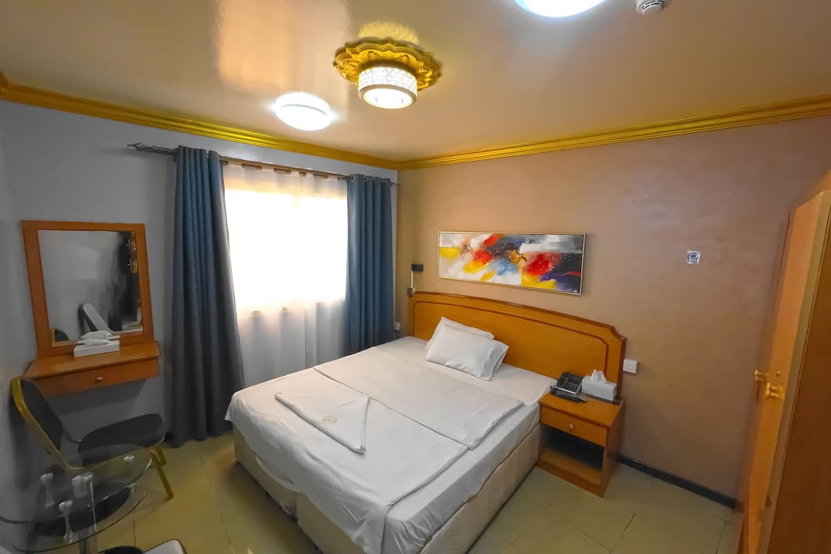 A hotel room with a bed, bedside table, nightstand, mirror, and a painting on the wall.