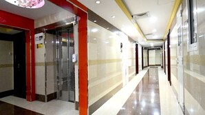 A hotel corridor with a shiny floor, red and beige walls, and a glass elevator. - Maaeen Hotel (Dubai)