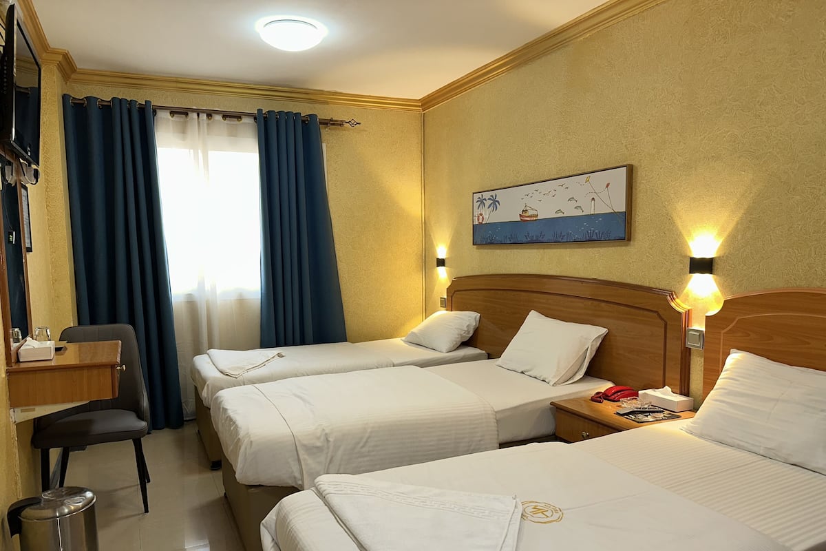 A hotel room with two beds, a desk, and a trash can.