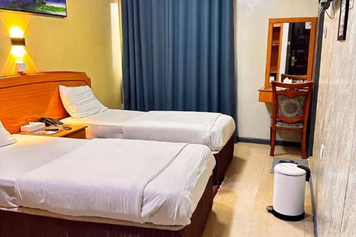A hotel room with two beds, a desk, a chair, a mirror, and a trash bin.