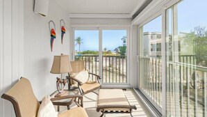 Ein sonnendurchfluteter Balkon mit Blick auf Strand und Meer, ausgestattet mit einem Stuhl, einem Tisch und einer Lampe.