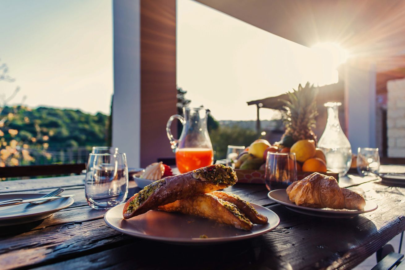 A breakfast table with croissants, a pitcher of juice, and a fruit bowl.