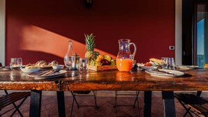 A wooden dining table set with plates, cutlery, a pitcher of orange juice, and a fruit basket. - Villa Clara – Country Retreat (Siracusa)