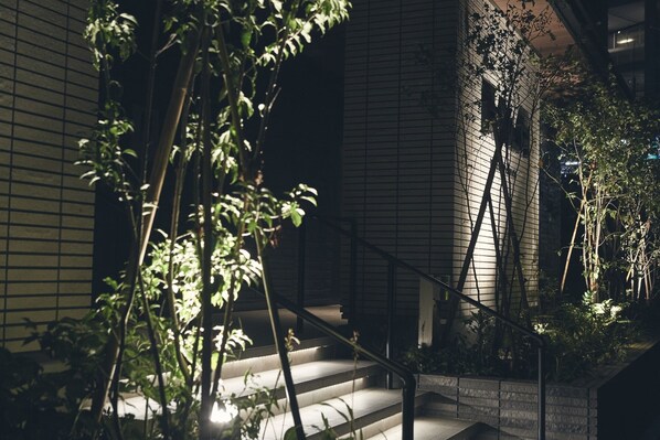 A staircase with a metal railing, surrounded by greenery and a building with a grid-like facade.