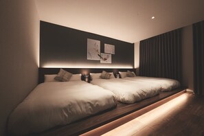 A modern hotel room with two beds, a dark wall with artwork, and a wooden floor.