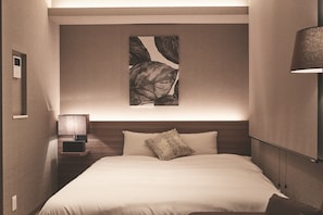 Quarto de hotel com cama, mesa de cabeceira com abajur, obra de arte na parede e luminária.
