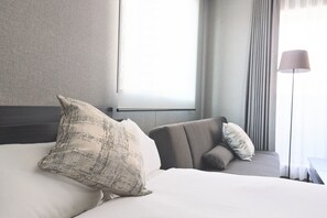 A hotel room with a large bed, a sofa, a lamp, and a window with curtains.