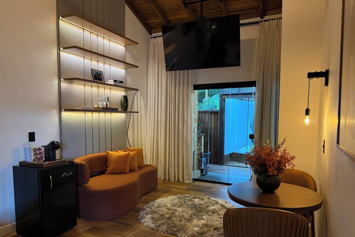 A modern living room with a sofa, a coffee machine, a TV, and a dining area with a table and chairs.