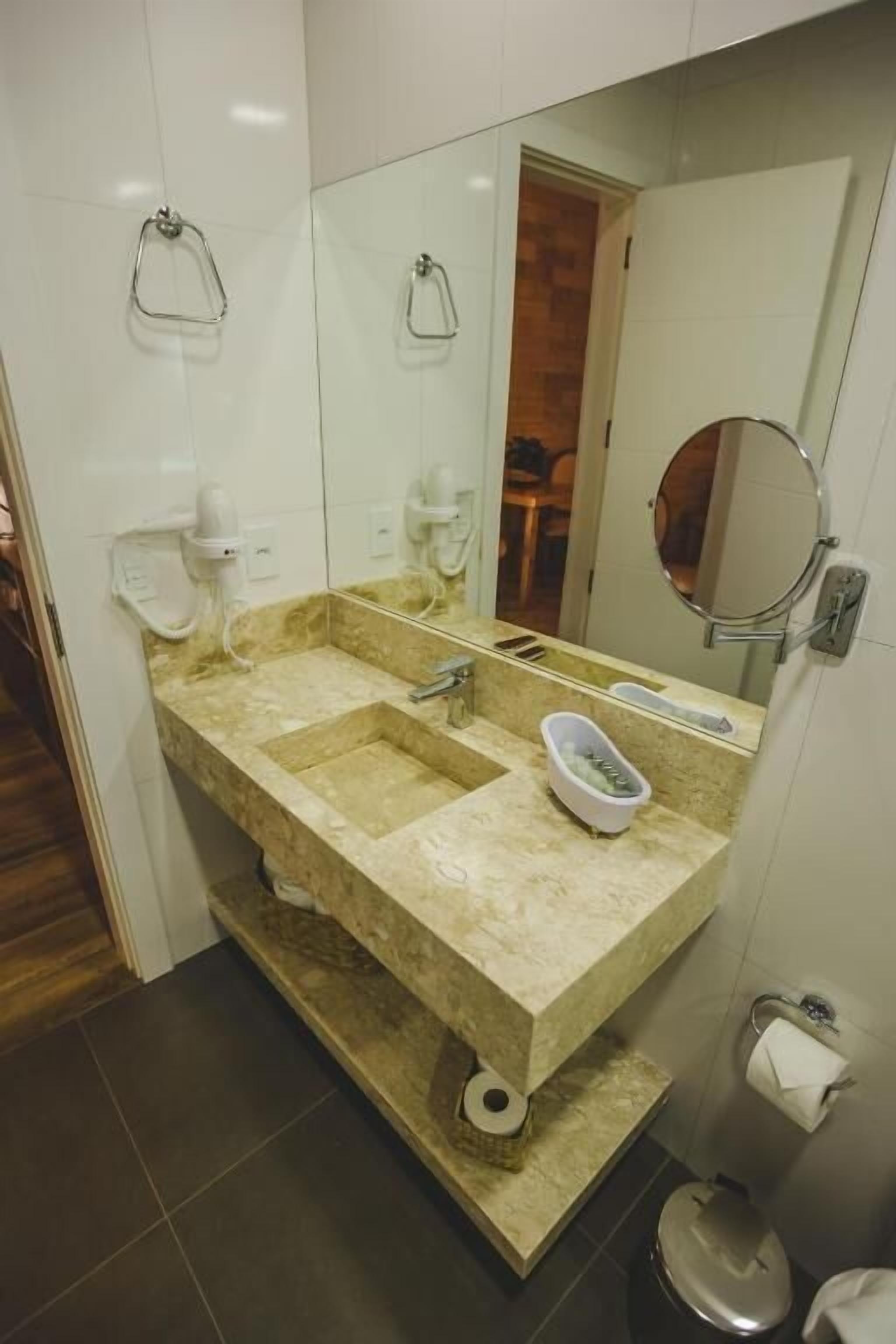 A bathroom with a beige marble sink, a mirror, a towel rack, and a toilet paper holder.