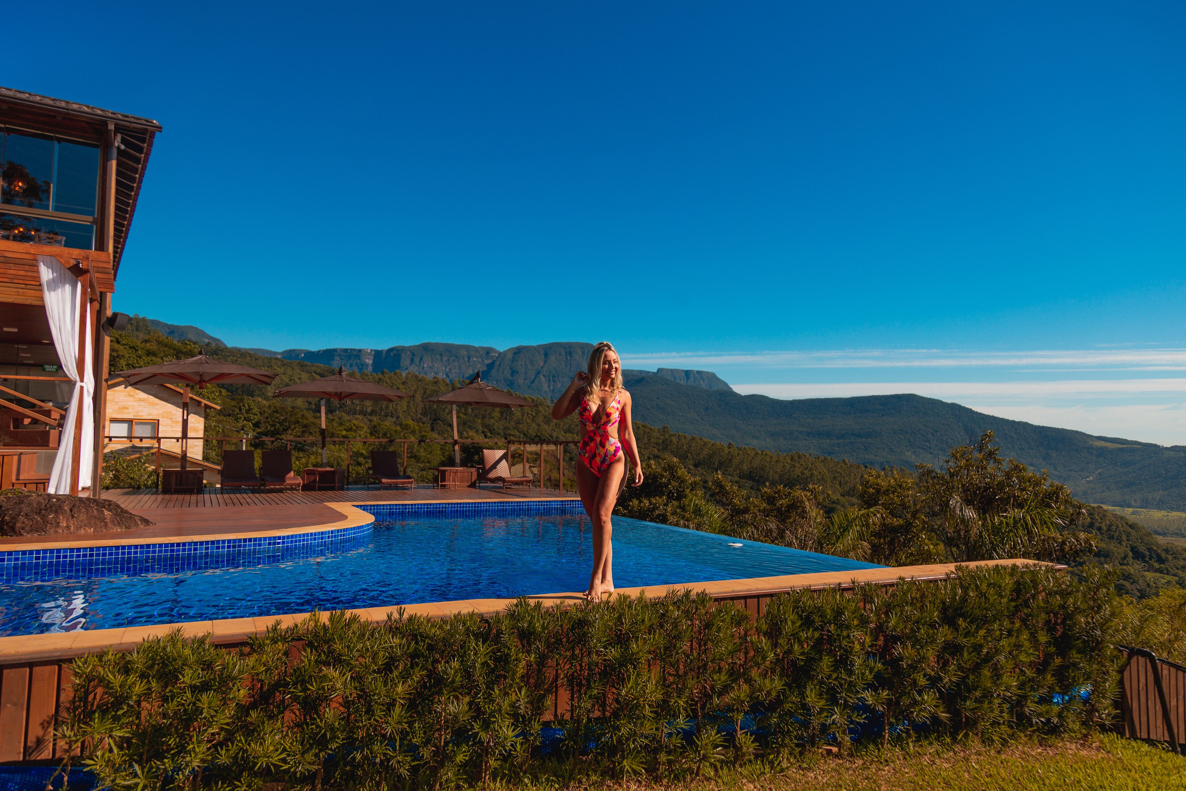 Una mujer en traje de baño de pie junto a una piscina, con vista a una montaña.