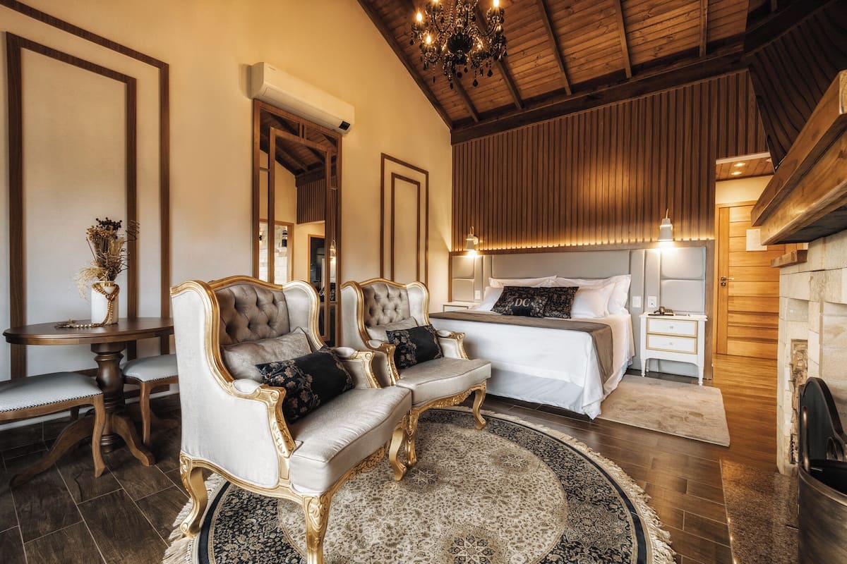 A luxurious bedroom with a large bed, two armchairs, a nightstand, and a chandelier.