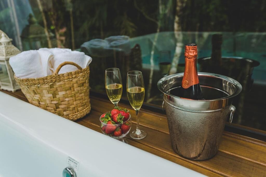 A wooden table with a woven basket, two glasses of champagne, a bucket with a bottle, and a bowl of strawberries.
