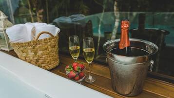 A wooden table with a woven basket, two glasses of champagne, a bucket with a bottle, and a bowl of strawberries.