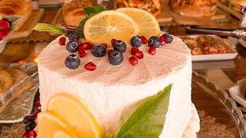 Un pastel de queso redondo con rodajas de limón y frutos rojos sobre un plato de vidrio.