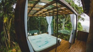 A hot tub in a wooden deck with a glass enclosure, surrounded by lush greenery. - Discovery Canyon (Praia Grande)