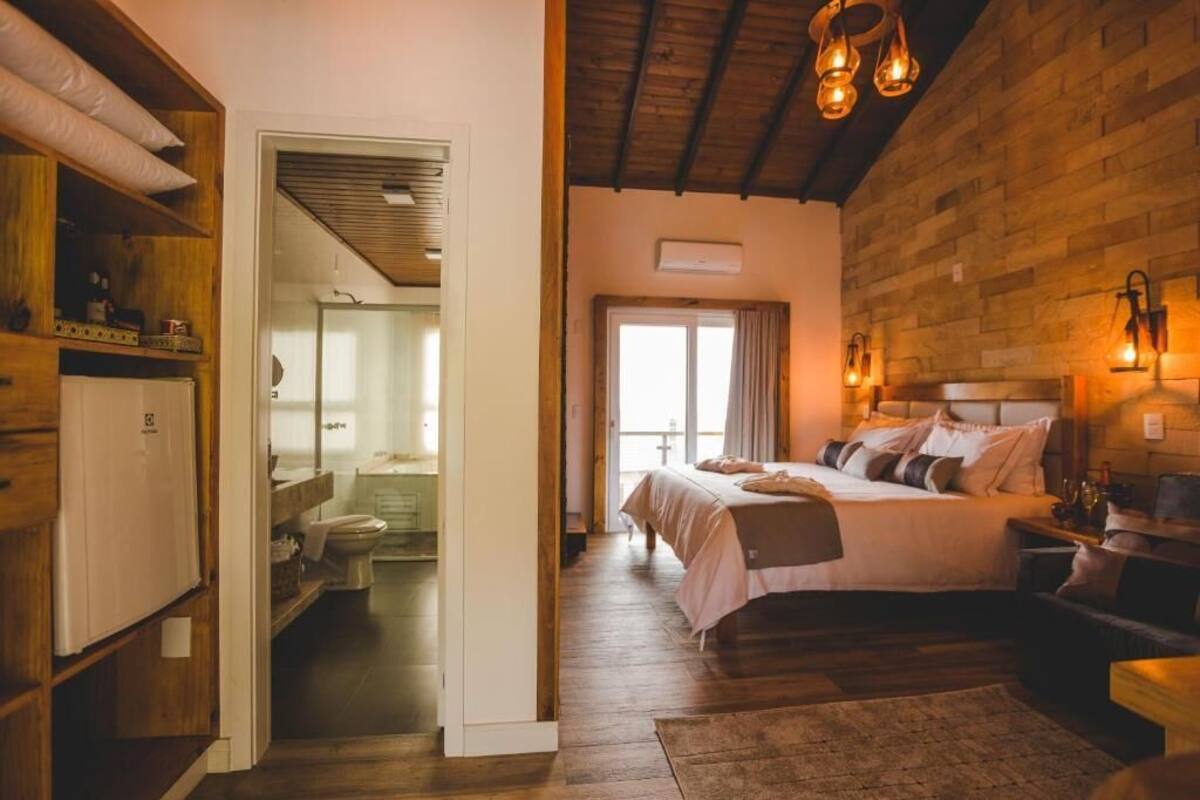 A bedroom with a wooden ceiling, a bed with multiple pillows, a nightstand, and a window with curtains.