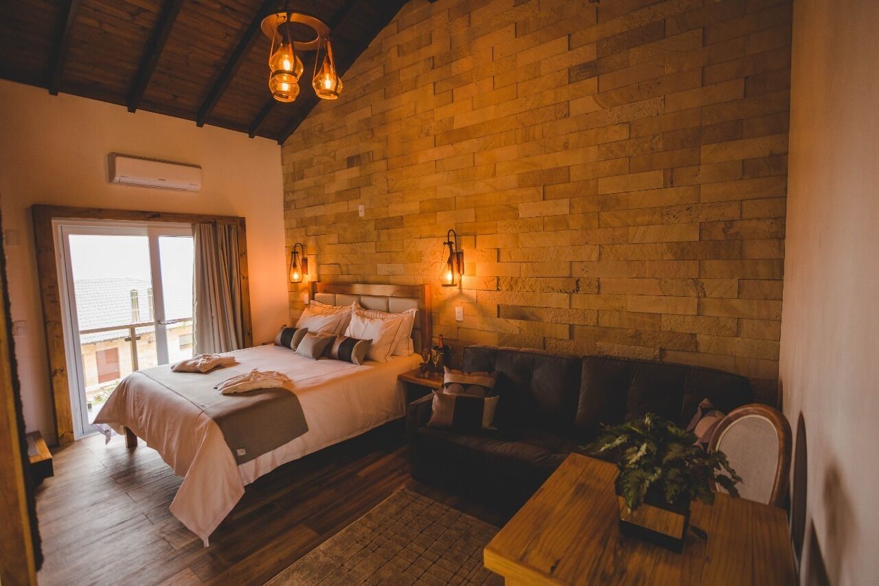 A bedroom with a large bed, a wooden ceiling, a brick wall, and a window.