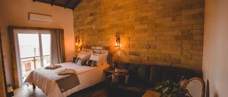 A bedroom with a large bed, a wooden ceiling, a brick wall, and a window.