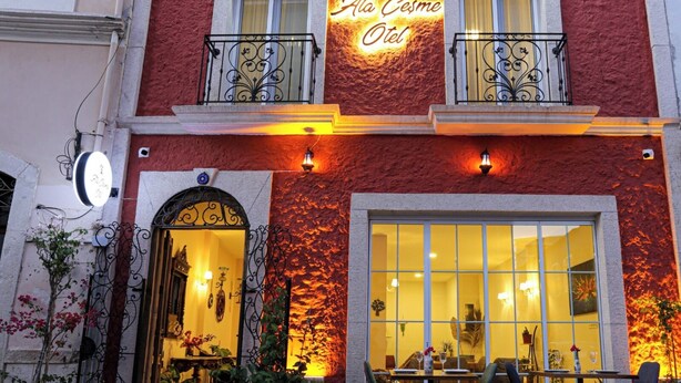 A hotel entrance with a red facade, a large glass window, outdoor seating, and a sign reading "Atto Cesme Otel". - ATAÇEŞME OTEL (Cesme)