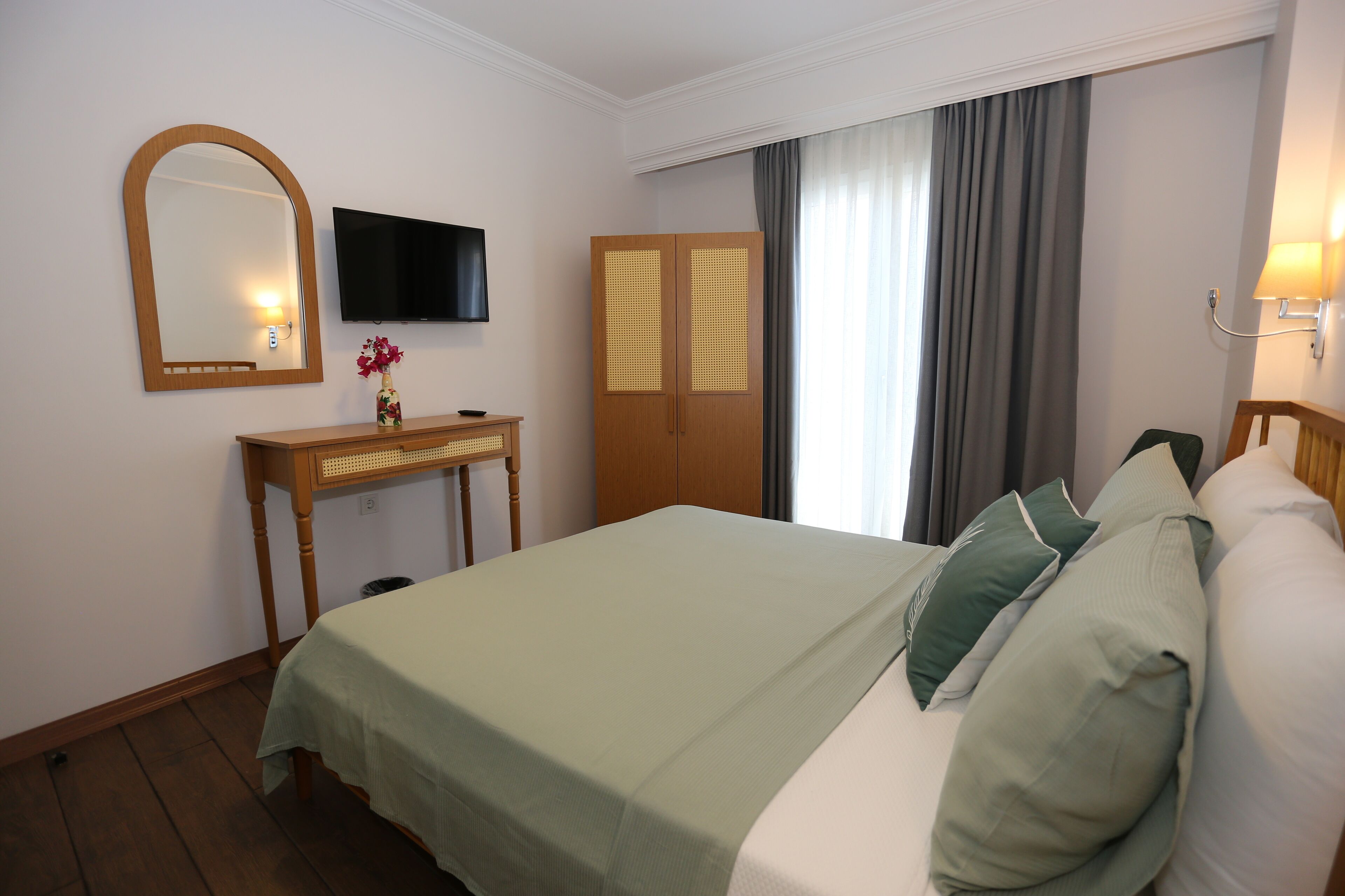 A hotel room with a bed, a wooden desk, a television, and a wardrobe.