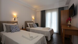 A hotel room with two beds, a desk, a TV, and a window with curtains. - ATAÇEŞME OTEL (Cesme)