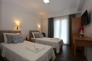A hotel room with two beds, a desk, a TV, and a window with curtains.