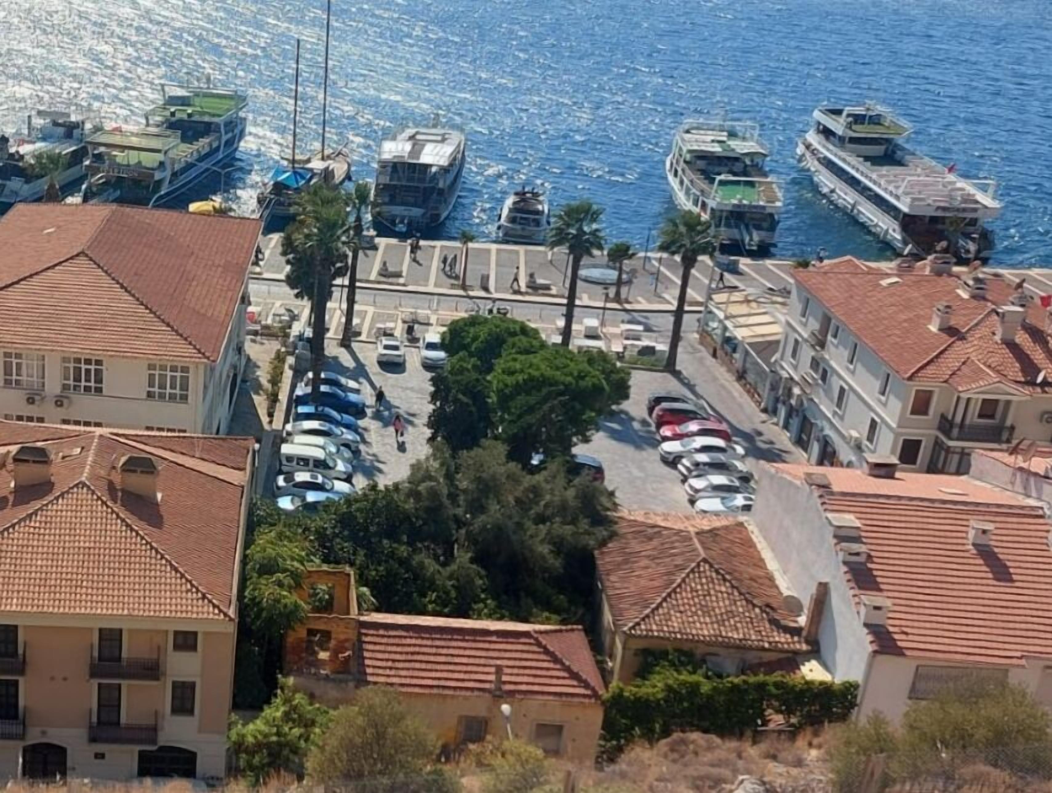 Un pueblo costero con un puerto deportivo, coches aparcados y edificios con tejados rojos.