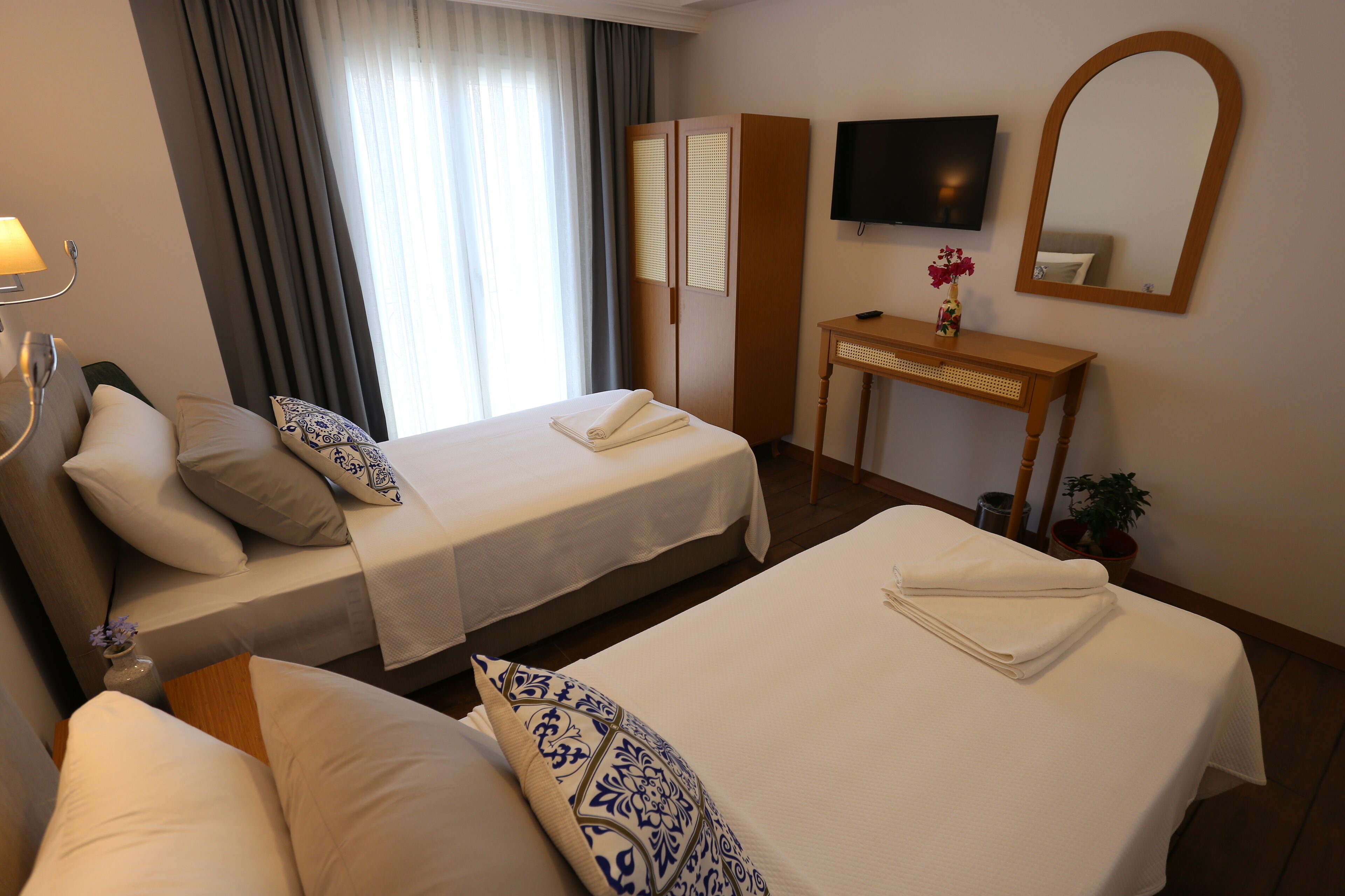 A hotel room with two beds, a desk, a TV, and a mirror.