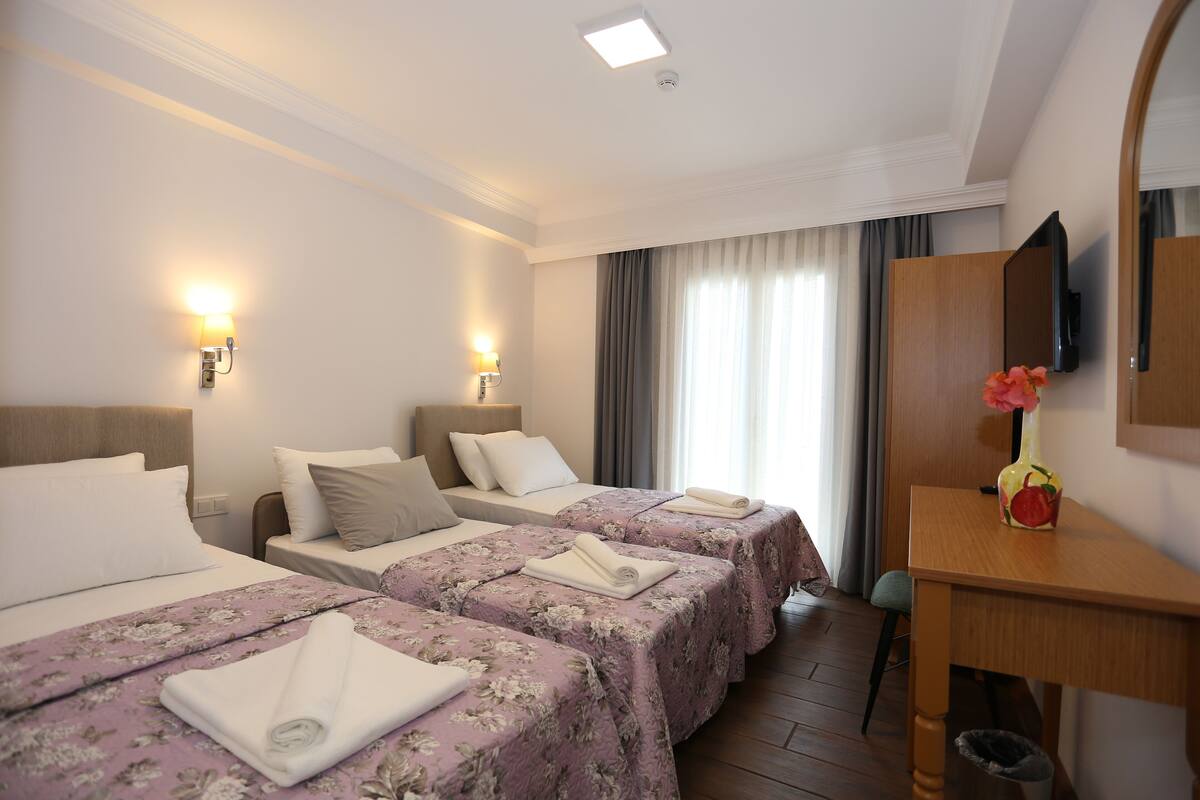 Une chambre d’hôtel avec deux lits, un bureau, une poubelle et un téléviseur fixé au mur.