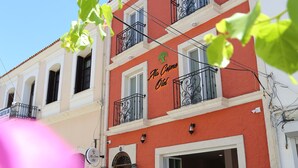 A two-story building with a red facade and balconies. The ground floor has a café with outdoor seating. - ATAÇEŞME OTEL (Cesme)
