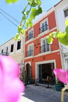 Un edificio de dos pisos con fachada roja y balcones. La planta baja tiene una cafetería con mesas al aire libre.