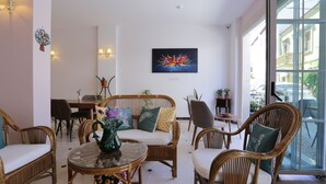 A modern interior with wicker furniture, a glass coffee table, and a large window offering a view of the street. - ATAÇEŞME OTEL (Cesme)