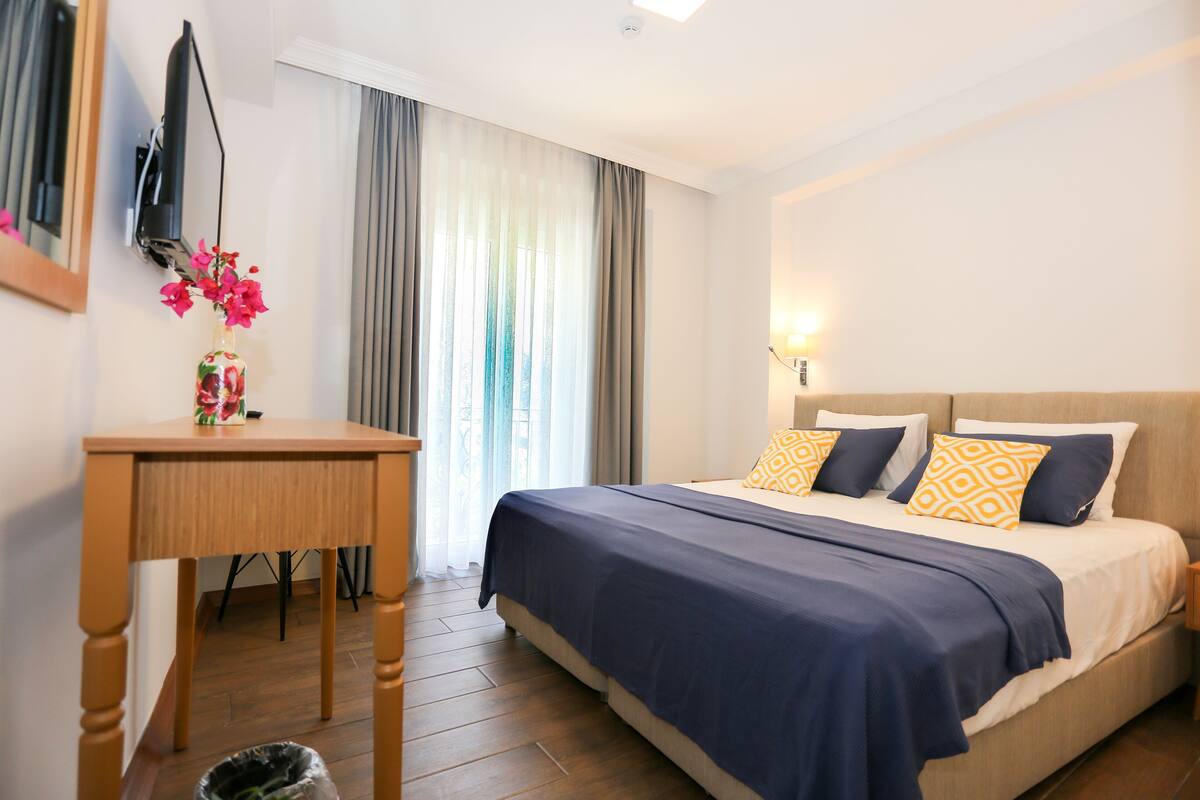 Une chambre d’hôtel équipée d’un lit, d’un bureau, d’une poubelle et d’un téléviseur fixé au mur.