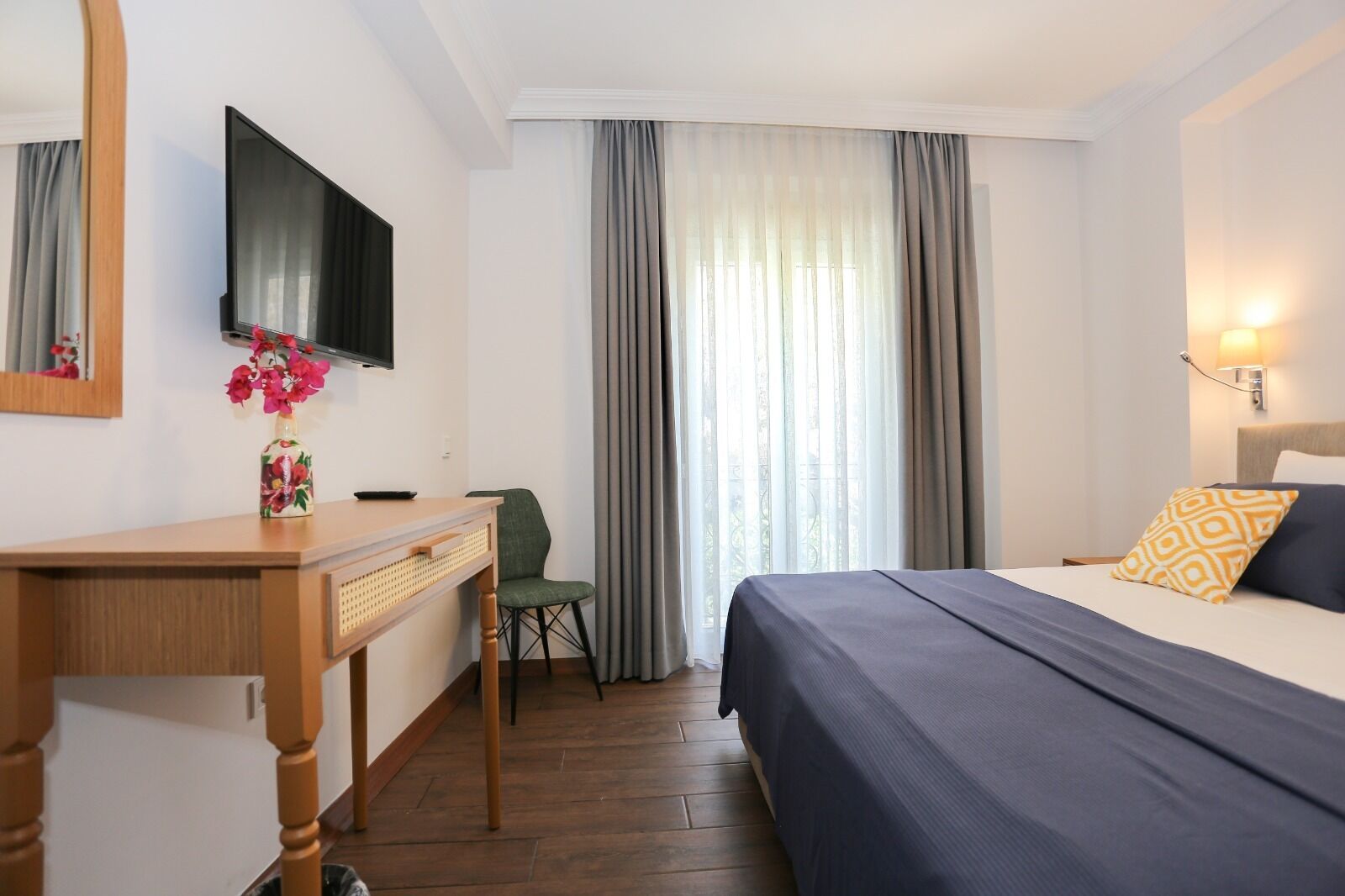A hotel room with a bed, a desk with a chair, a television, and a window with curtains.