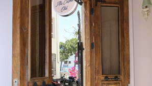 An open wooden door with a sign above it, a potted plant to the right, and a vehicle parked outside. - ATAÇEŞME OTEL (Cesme)