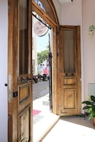 Una puerta de madera abierta con un letrero encima, una planta en maceta a la derecha y un vehículo estacionado afuera.