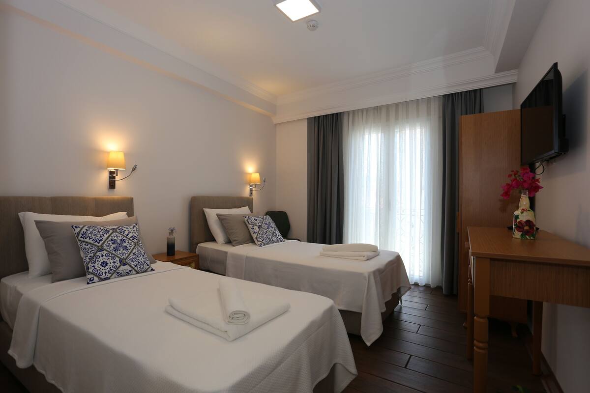 Une chambre d’hôtel avec deux lits, un bureau, une télévision et une fenêtre avec des rideaux.