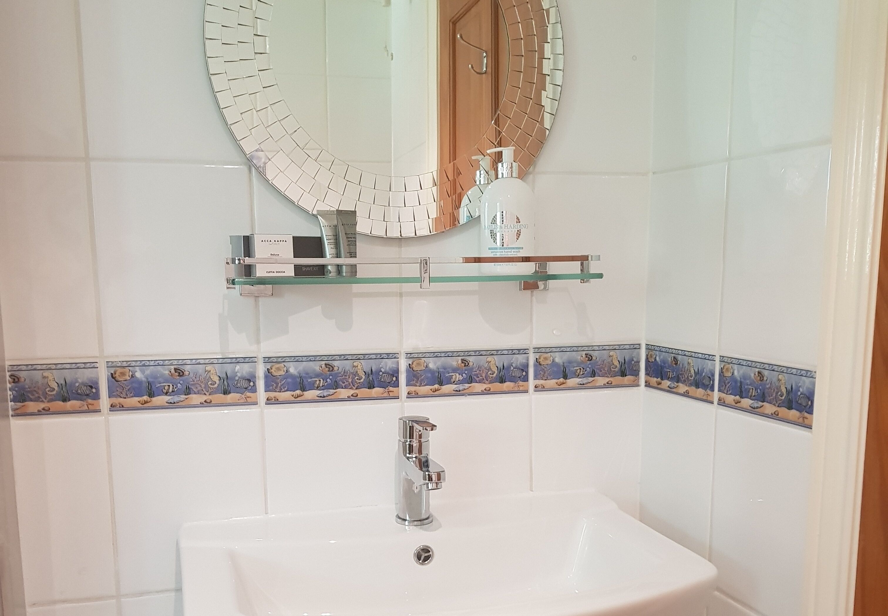 A bathroom with a white sink, a mirror with a mosaic border, and a shelf with toiletries.